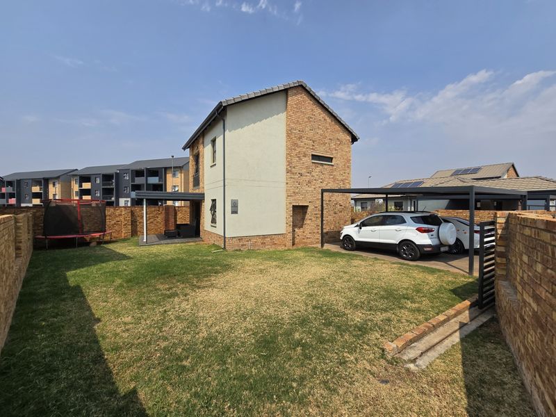 Rear view of the property featuring a private garden, covered patio area, and a dedicated carport structure.