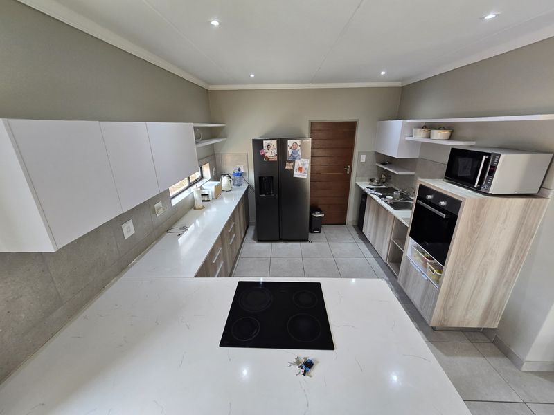 Modern kitchen featuring white quartz countertops, built-in oven, electric hob, ample cabinetry, and tiled flooring in a functional U-shaped layout.