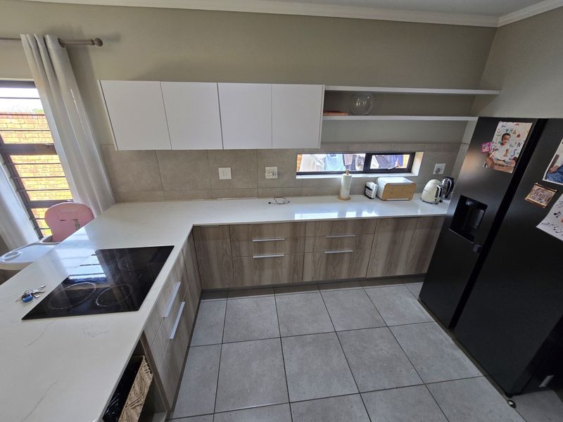 Modern kitchen featuring wood-grain cabinetry, white stone countertops, an integrated electric hob, and neutral tiled flooring with a functional layout.