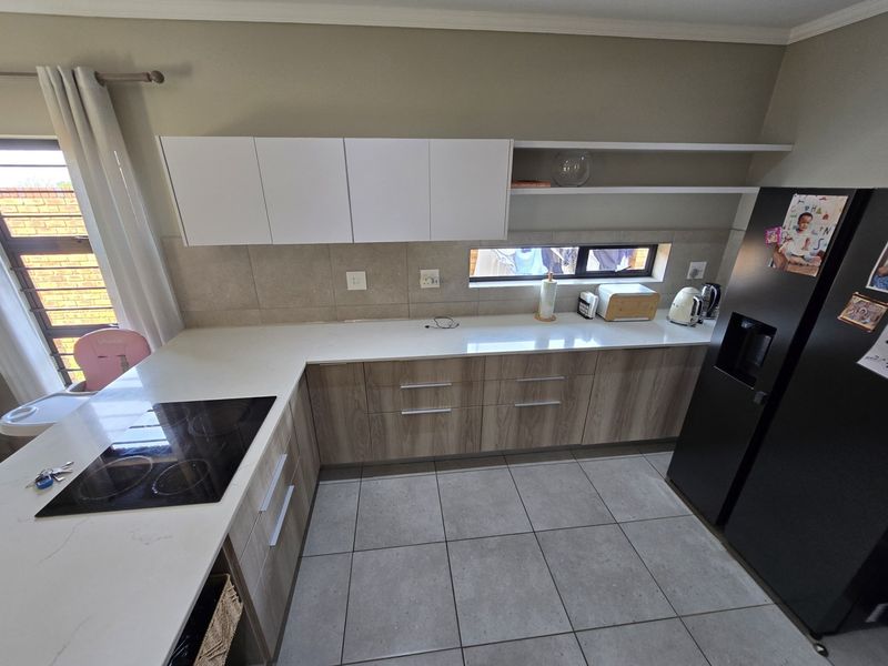 Modern kitchen featuring light wood-grain cabinetry, white stone countertops, a built-in electric hob, and neutral tiled flooring with a sleek backsplash.