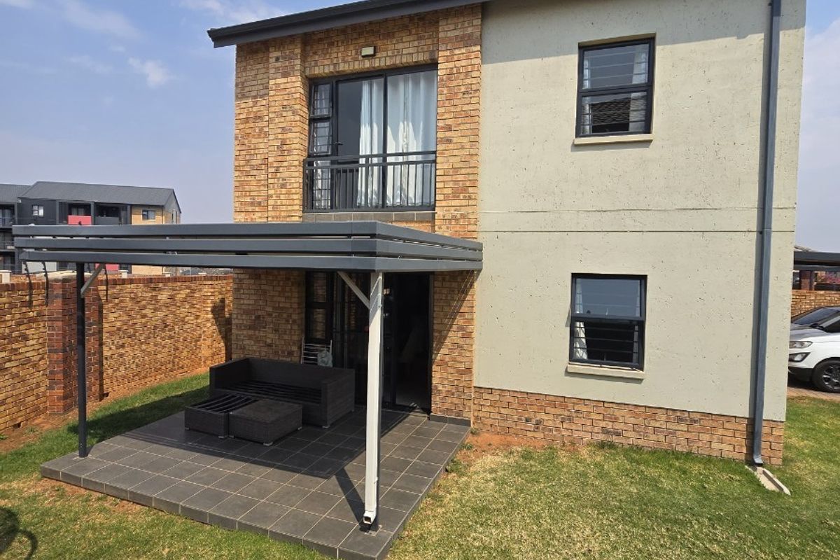 Rear view of a two-story house featuring a tiled patio with a pergola, brick and plastered exterior walls, and an upper-level balcony.