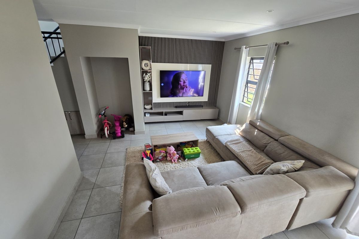 A modern living room featuring a built-in media unit with a slatted feature wall, tiled flooring, and recessed ceiling lighting.
