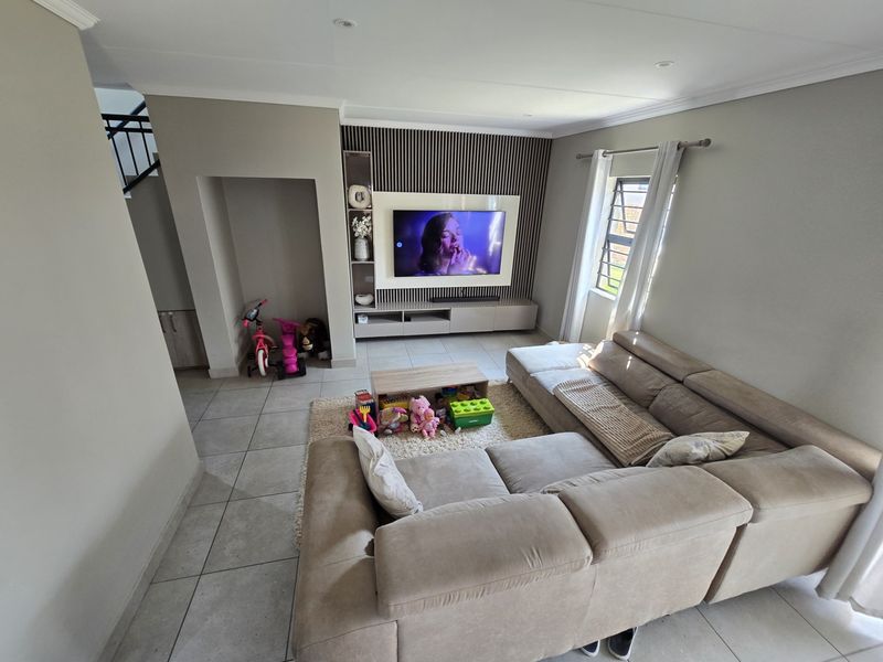 A modern living room featuring a built-in media unit with a slatted feature wall, tiled flooring, and recessed ceiling lighting.