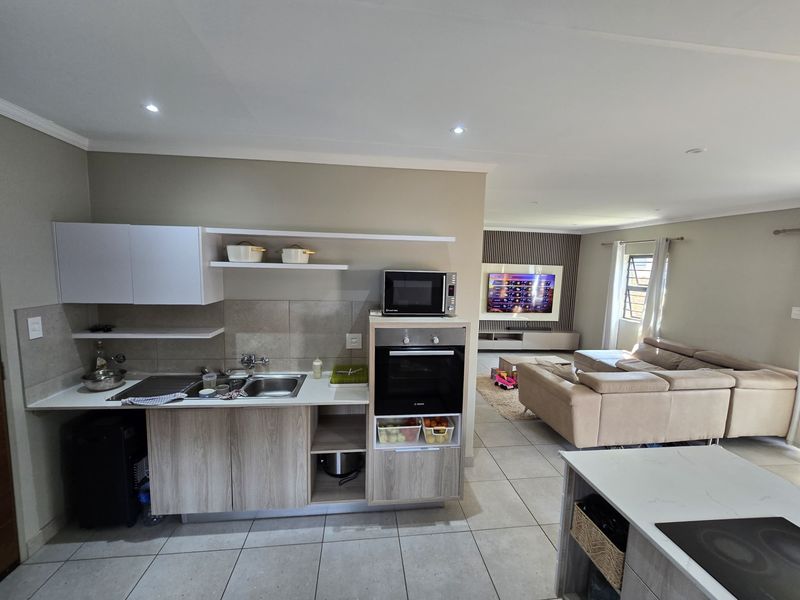 Modern open-plan living area featuring a contemporary kitchen with built-in appliances, stone countertops, and seamless flow into the spacious lounge with feature wall.