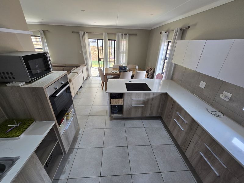 Modern open-plan kitchen and living area featuring contemporary cabinetry, stone countertops, integrated appliances, and direct access to the outdoor patio through sliding doors.