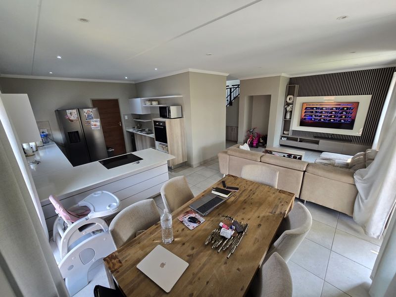 Spacious open-plan living area featuring a modern kitchen with island, dining space, and a built-in media wall, finished with neutral tones and tiled flooring.