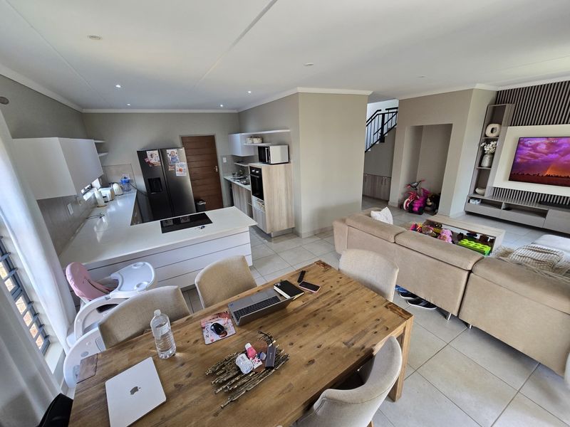 Spacious open-plan living area featuring a modern kitchen with island, dining space, and a built-in media wall, finished with neutral tones and tiled flooring.