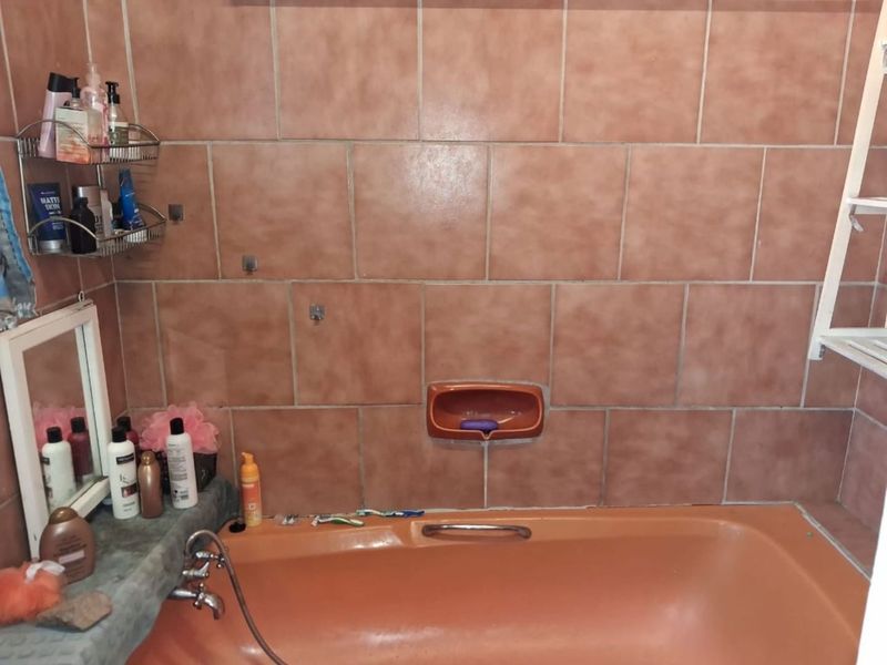A bathroom featuring a built-in bathtub with dated ceramic wall tiles and a recessed soap dish.
