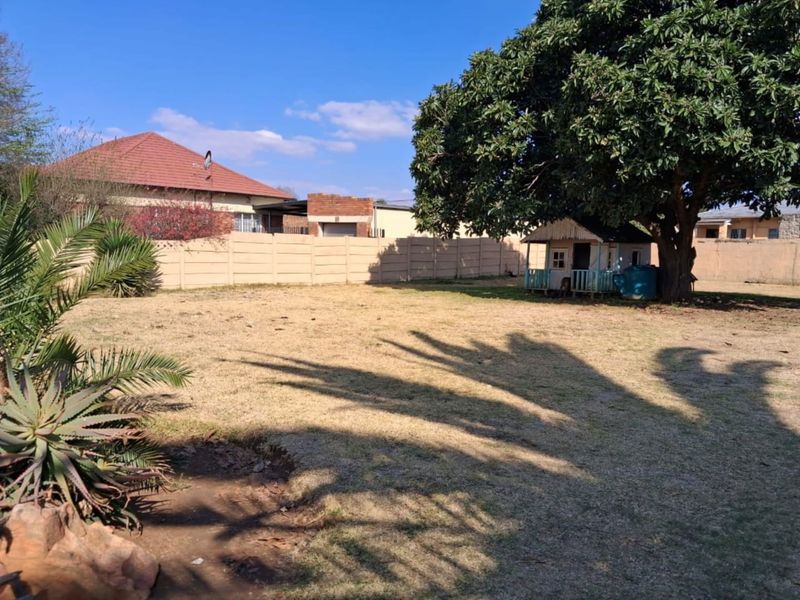A spacious backyard featuring a large mature tree, a small wooden playhouse, and a secure precast concrete boundary wall.