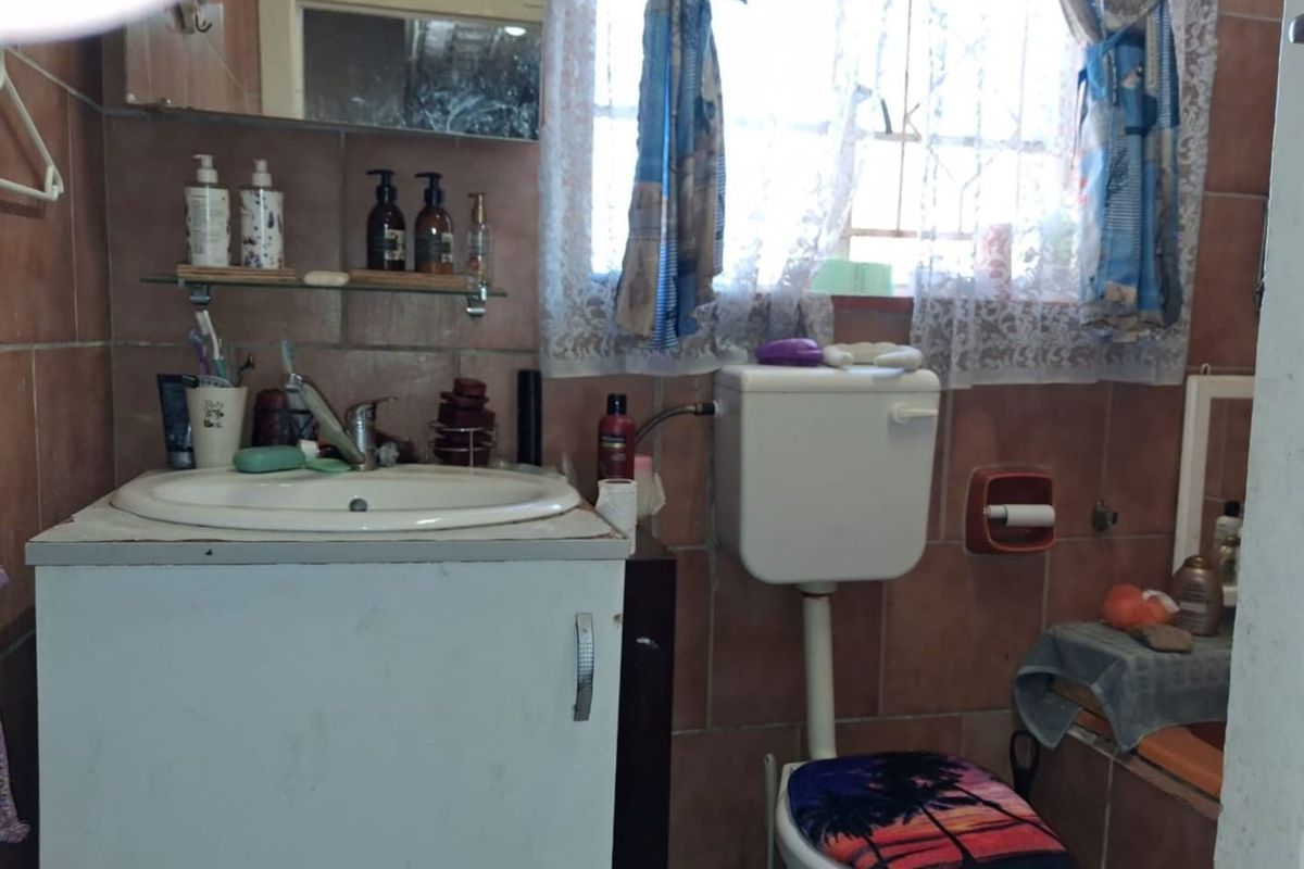 A dated bathroom featuring a vanity cabinet, ceramic basin, and toilet with full-height wall tiling and a window for natural light.
