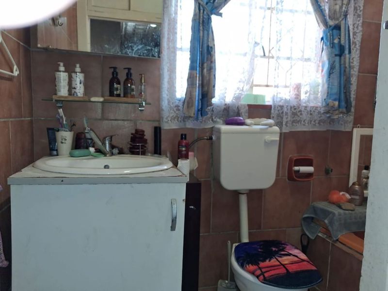 A dated bathroom featuring a vanity cabinet, ceramic basin, and toilet with full-height wall tiling and a window for natural light.