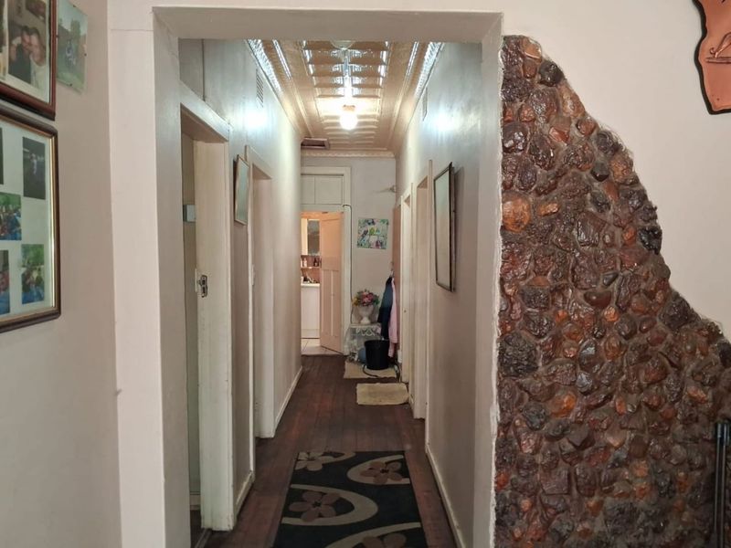 A long hallway featuring a unique exposed stone feature wall, traditional pressed metal ceiling, and timber flooring leading towards the rear of the home.