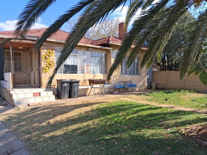 Rear view of a single-story house featuring a tiled roof, brick chimney, and a concrete patio area overlooking a garden with boundary walling.