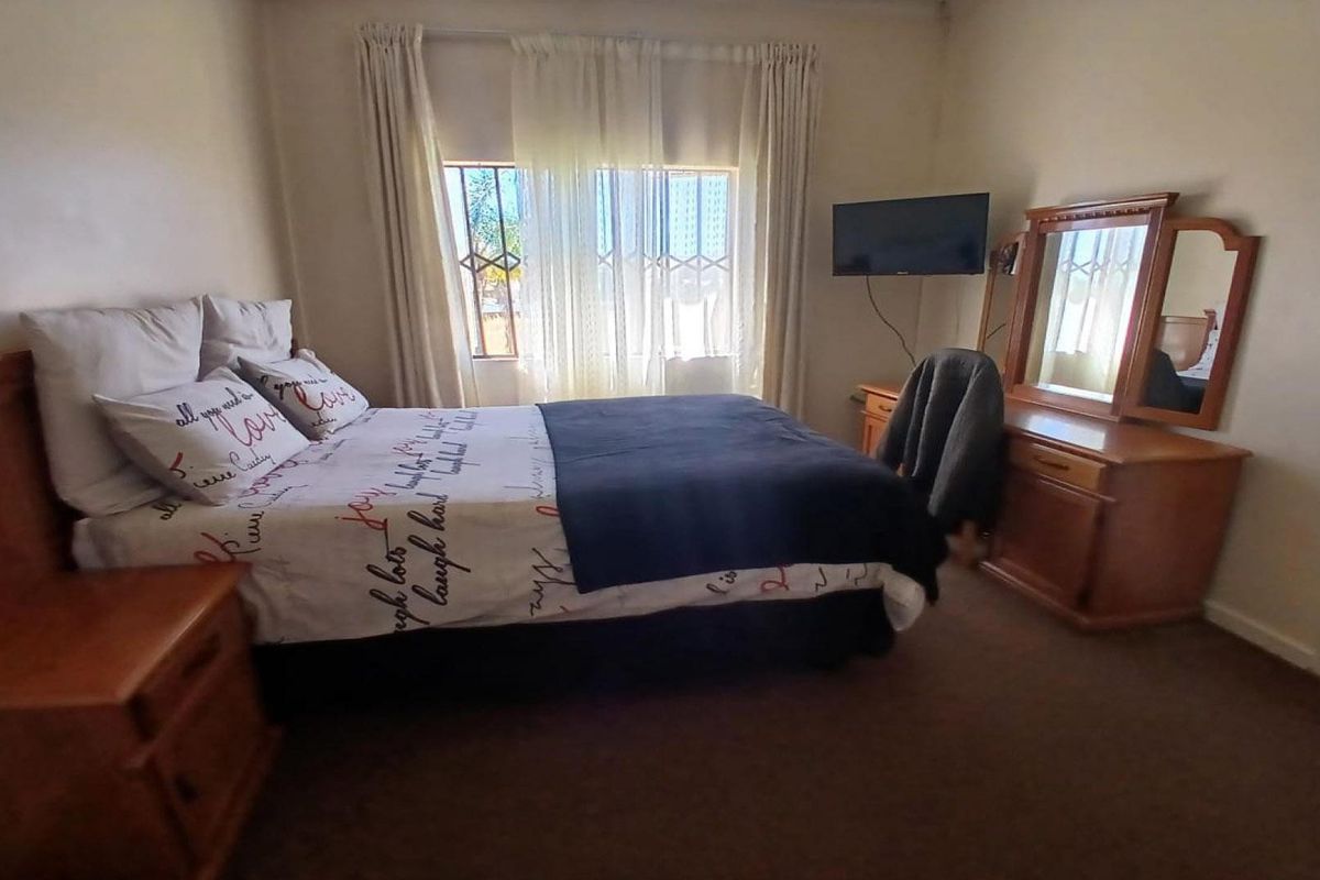 A standard bedroom featuring carpeted flooring and a window fitted with security bars.