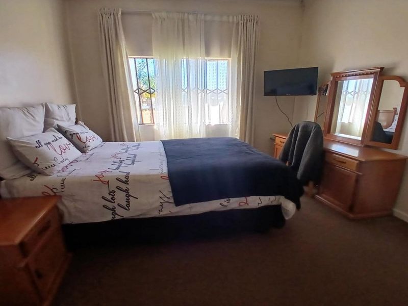 A standard bedroom featuring carpeted flooring and a window fitted with security bars.