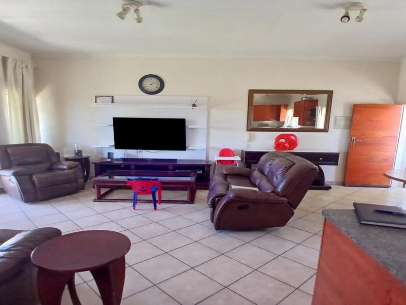 Spacious open-plan living area featuring tiled flooring, a built-in media unit, and direct access to an outdoor patio through sliding glass doors.