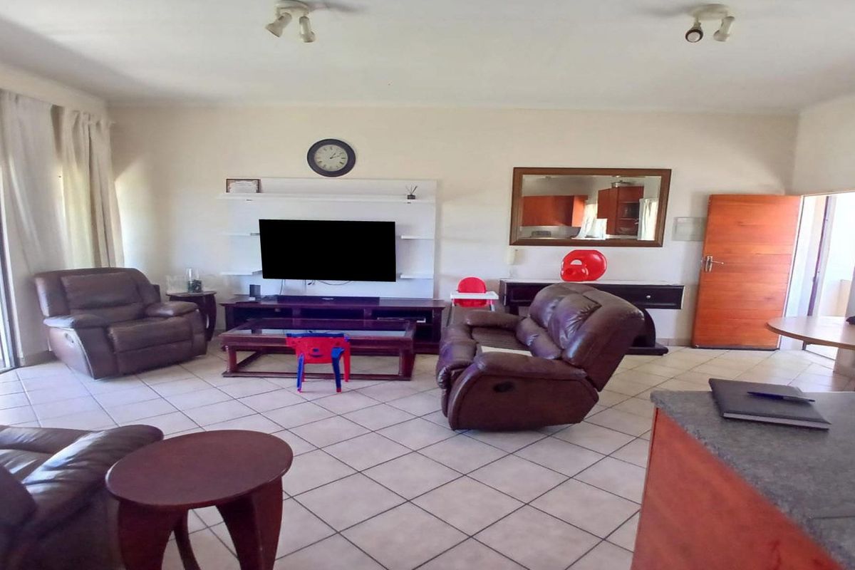 Spacious open-plan living area featuring tiled flooring, a built-in media unit, and direct access to an outdoor patio through sliding glass doors.