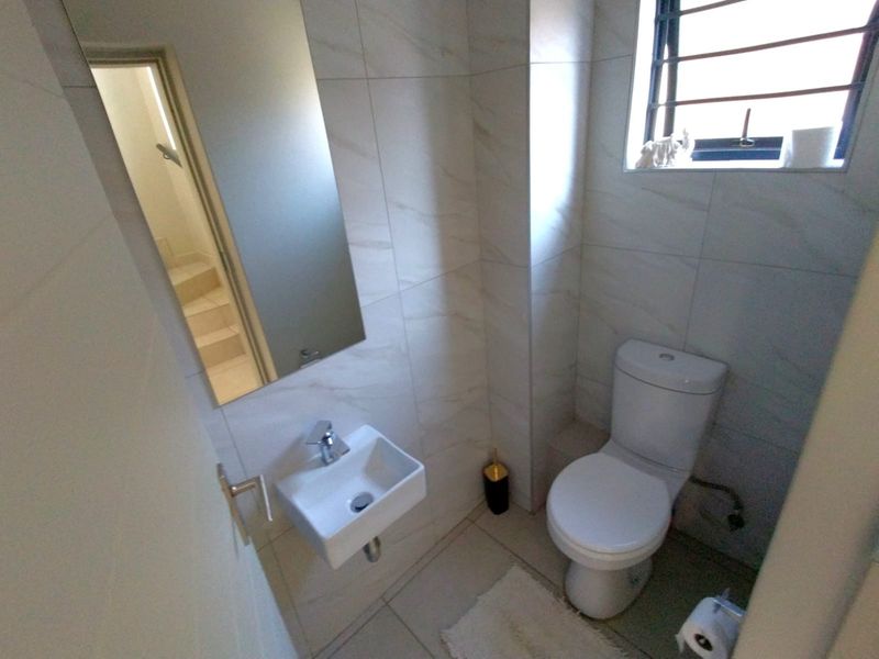 A compact, modern guest bathroom featuring tiled walls, a wall-mounted basin, and a standard toilet.