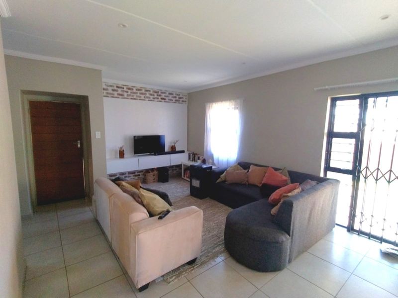 A well-maintained living room featuring tiled flooring, an exposed brick feature wall, and a built-in media console with natural light from the window.
