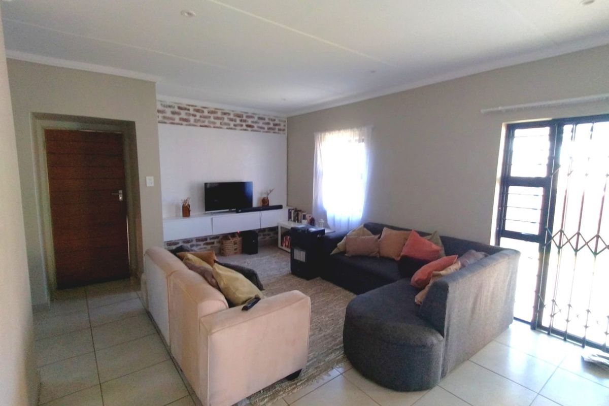 A well-maintained living room featuring tiled flooring, an exposed brick feature wall, and a built-in media console with natural light from the window.
