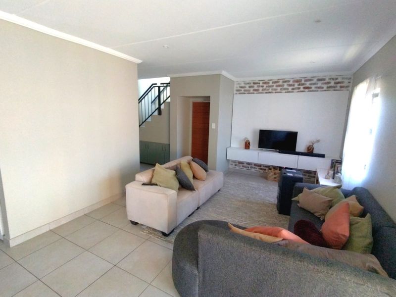 Spacious living room featuring tiled flooring, a built-in media console, and an exposed brick feature wall, with an adjacent staircase leading to the upper level.