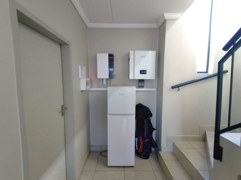 Utility area featuring a wall-mounted inverter and battery storage system, adjacent to a staircase with a modern handrail and tiled flooring.