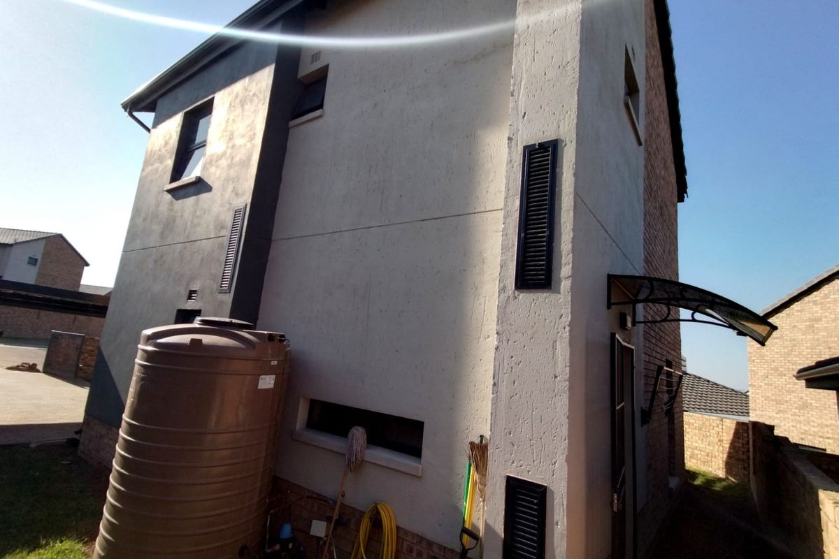 Rear exterior view of the townhouse featuring a water storage tank, plastered walls, and a small entrance awning.