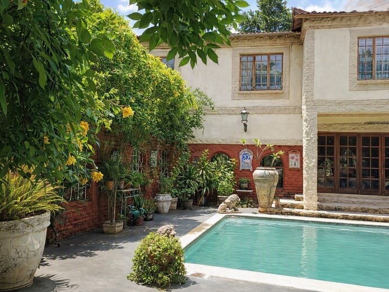 A charming courtyard pool area featuring rustic brick walls, stone-clad architectural details, and mature greenery, creating a tranquil outdoor entertainment space.
