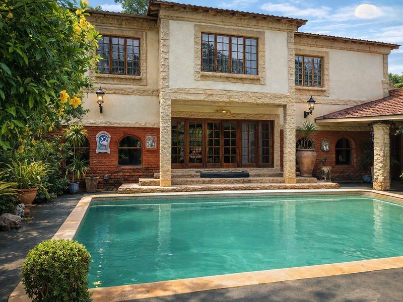 A well-maintained rear exterior view featuring a swimming pool, stone-clad facade, and classic timber-framed doors and windows.