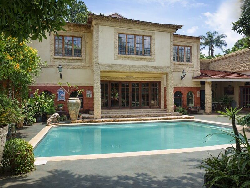 A well-maintained swimming pool area featuring stone and brick facade detailing, timber-framed windows, and a covered patio space.