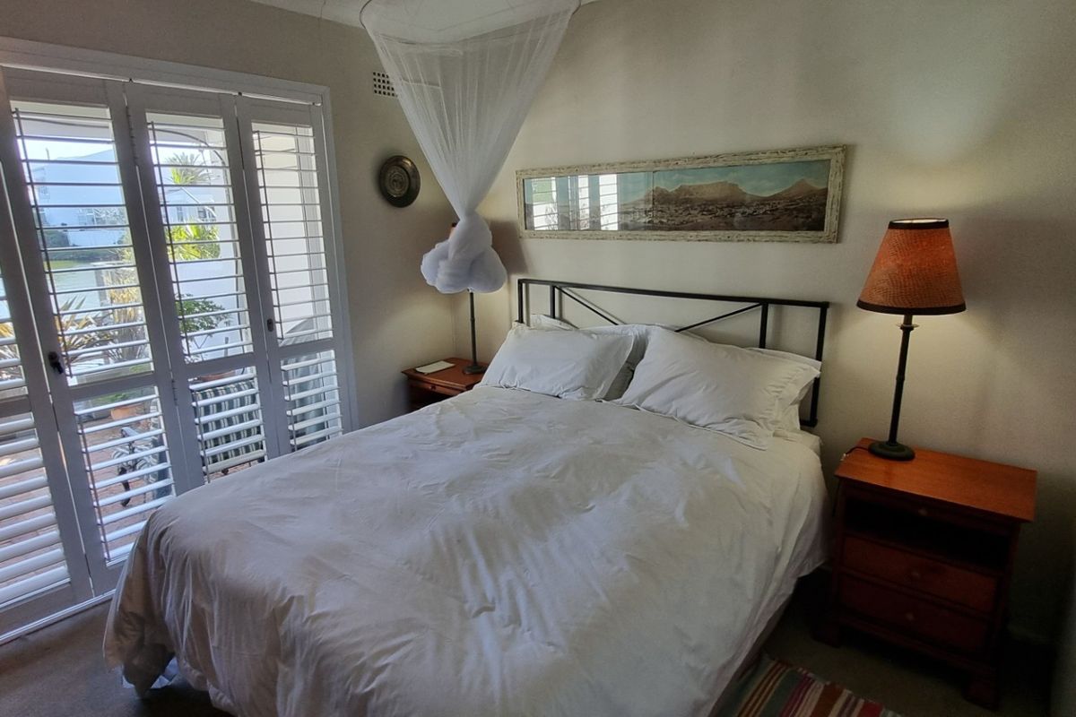 A cozy bedroom featuring built-in wardrobes and white plantation shutters that open onto an outdoor area.