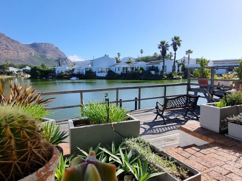 A scenic outdoor patio featuring wooden decking and a timber railing, offering beautiful views of the adjacent lake and surrounding mountain landscape.