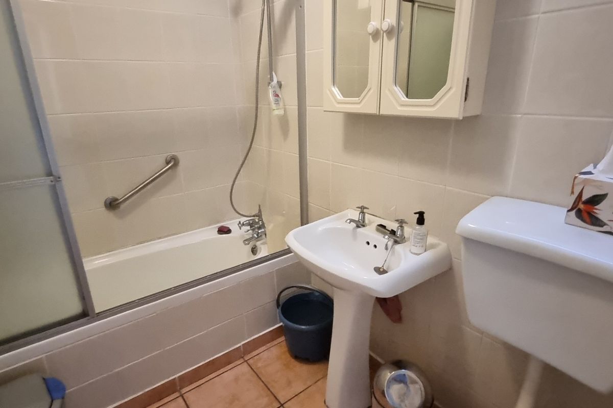 A functional bathroom featuring a pedestal basin, a bathtub with a shower mixer, and a toilet, finished with neutral wall and floor tiles.