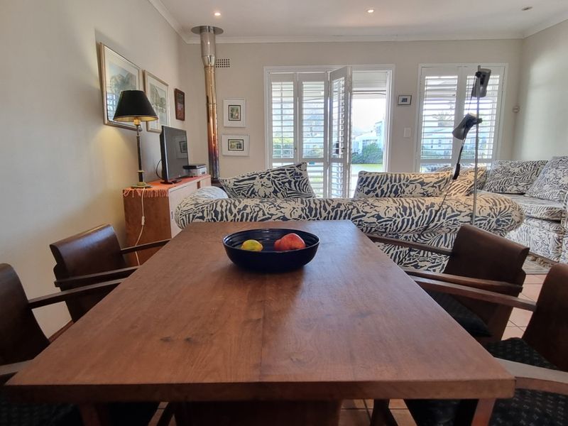 Open-plan living and dining area featuring tiled flooring, a wood-burning fireplace, and plantation shutters opening to an outdoor space.