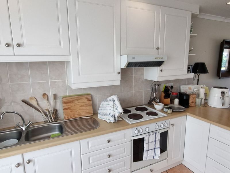 Functional kitchen featuring white cabinetry, laminate countertops, tiled backsplash, and integrated appliances including an electric hob and oven.