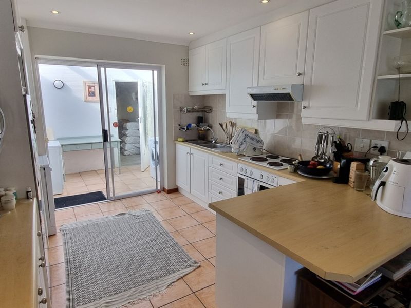 A functional kitchen featuring white cabinetry, an electric hob, and tiled flooring, with direct access through a sliding door to an adjacent utility area.