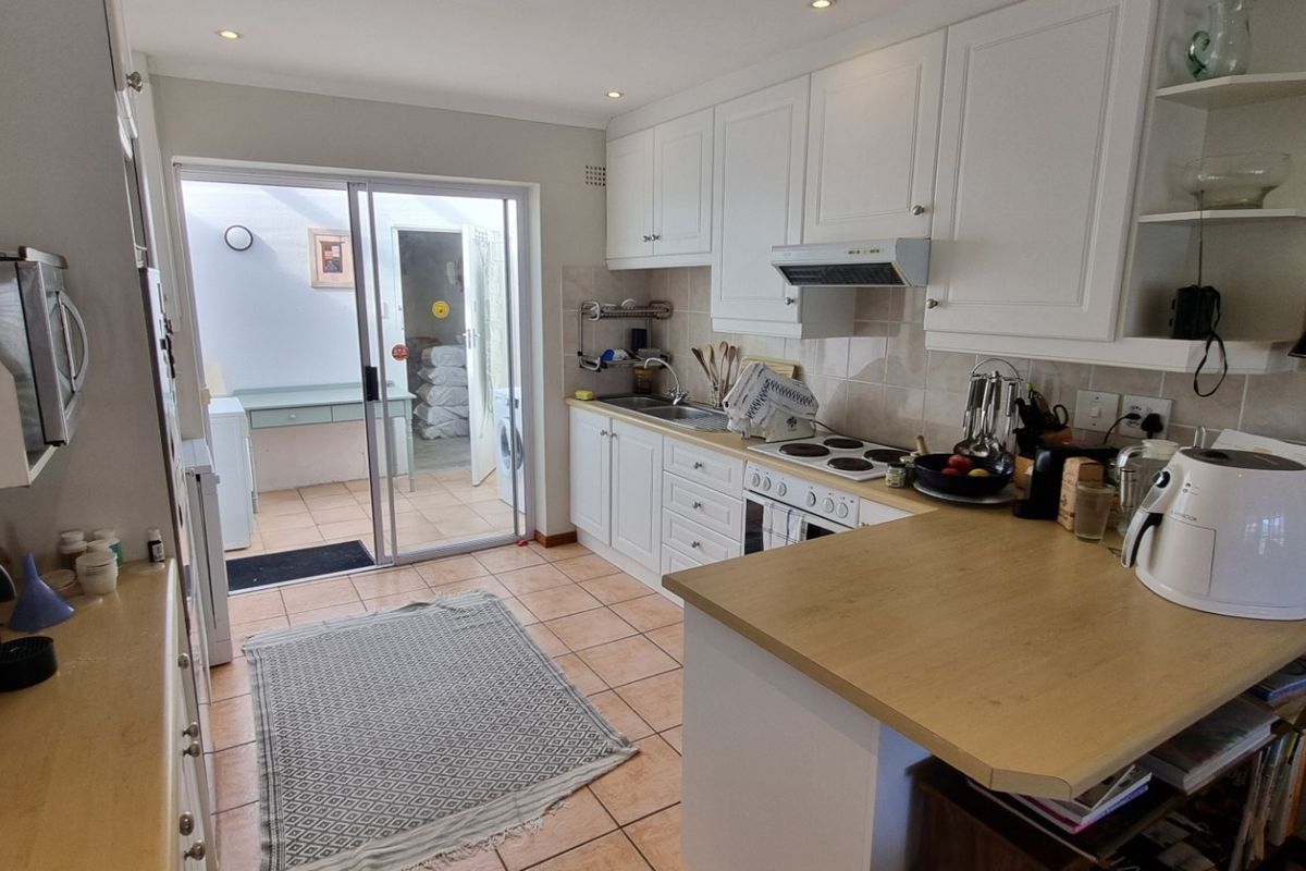 A functional kitchen featuring white cabinetry, an electric hob, and tiled flooring, with direct access through a sliding door to an adjacent utility area.