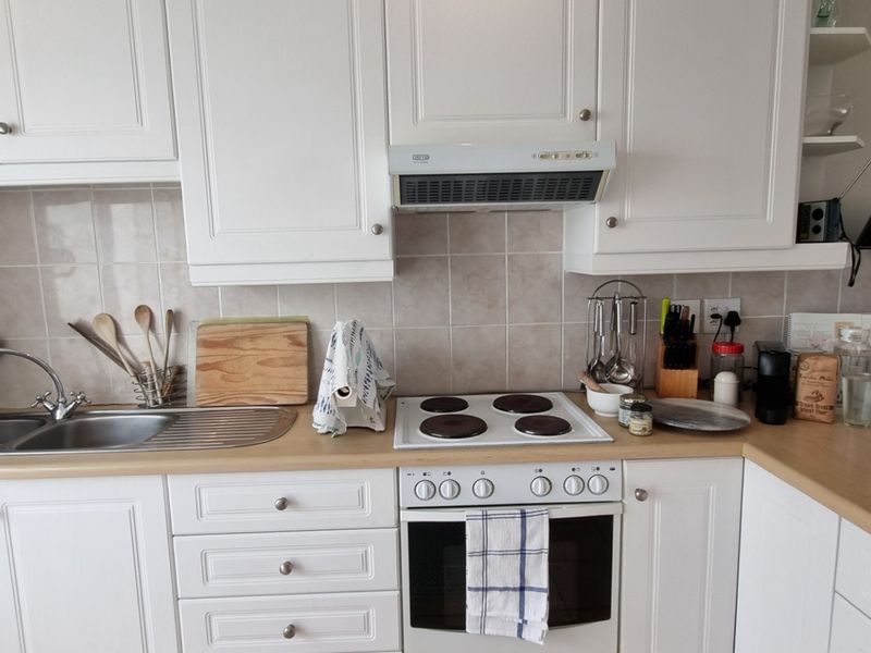 A functional kitchen featuring white cabinetry, laminate countertops, a stainless steel double sink, and integrated cooking appliances with a tiled backsplash.