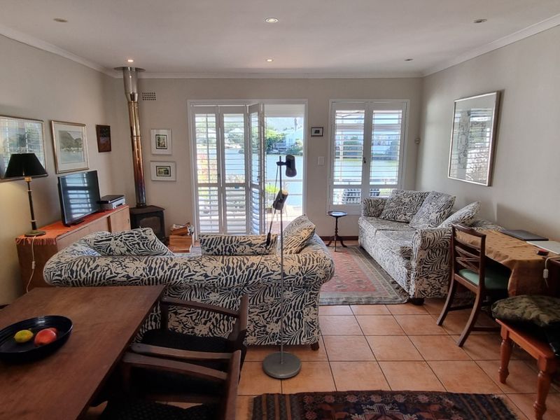 A comfortable living room featuring tiled flooring, a freestanding fireplace, and plantation shutters opening to a scenic outdoor view.