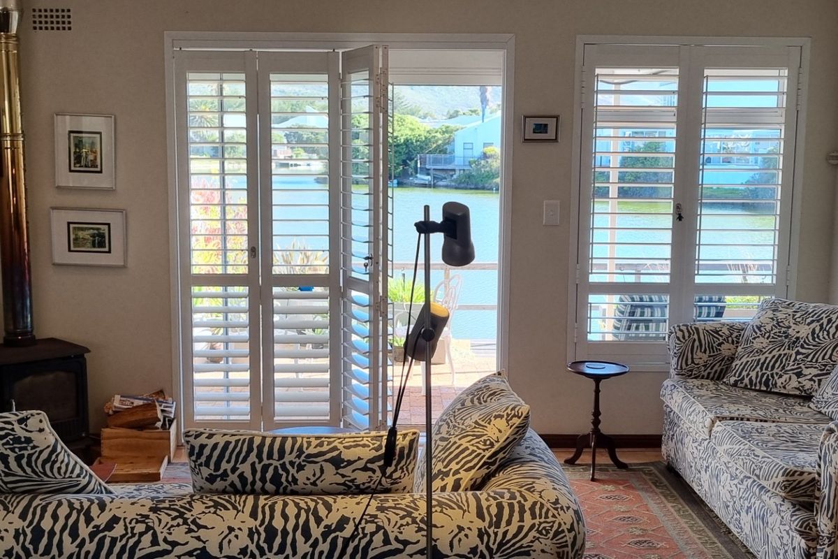 Cozy living room featuring a wood-burning fireplace and plantation shutters, with direct access to a patio overlooking the water.