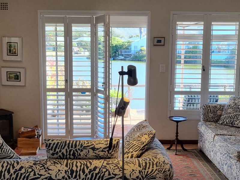 Cozy living room featuring a wood-burning fireplace and plantation shutters, with direct access to a patio overlooking the water.