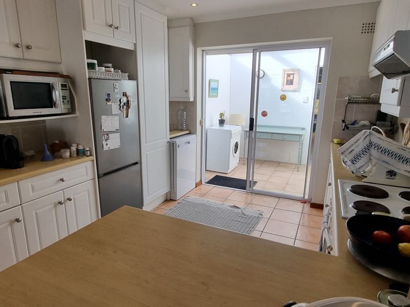 A functional kitchen featuring white cabinetry, laminate countertops, an electric hob with extractor, and direct access to an outdoor utility area via sliding doors.
