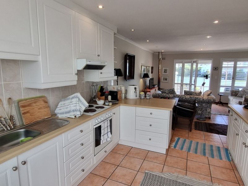 Open-plan kitchen and living area featuring white cabinetry, tiled flooring, and direct access to the outdoor space through glass french doors.