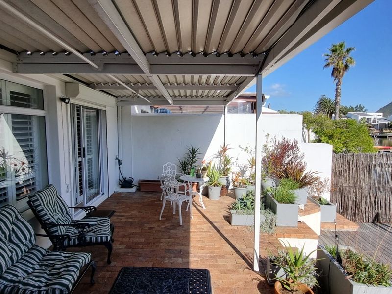Covered patio featuring brick flooring and a corrugated metal roof, overlooking a tranquil waterfront area with mountain views.