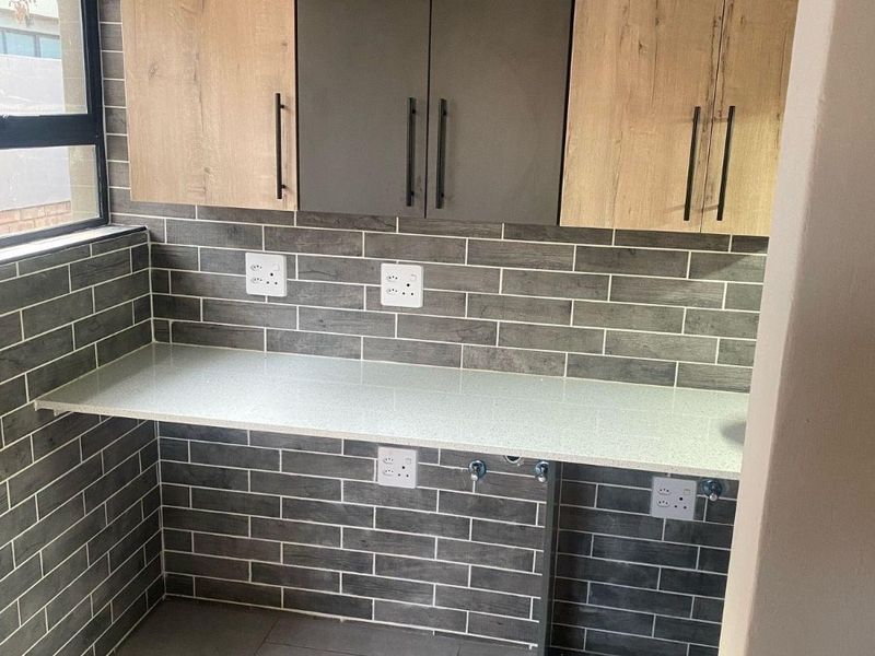 A modern, clean laundry area featuring contemporary two-tone cabinetry, stone countertops, and stylish grey subway tile backsplash with dedicated plumbing and electrical points.