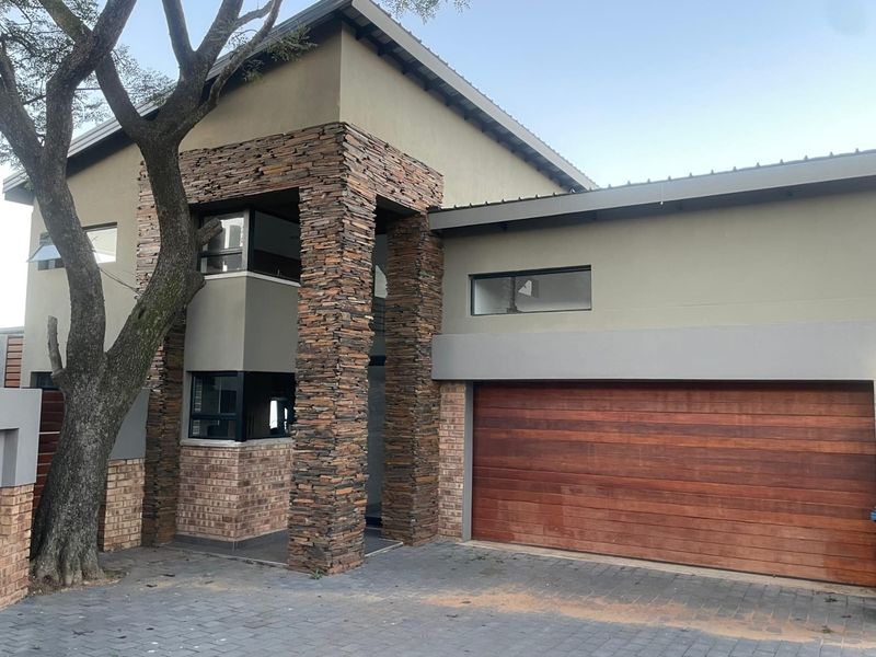 Modern double-storey residential facade featuring stone cladding, brick accents, and a timber garage door with a paved driveway.