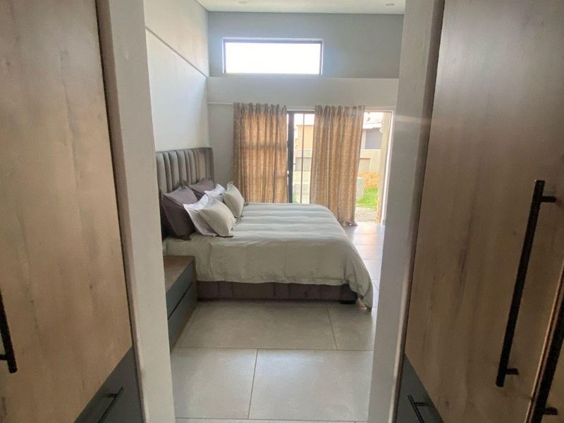 A modern bedroom featuring built-in cupboards, large format floor tiles, and a clerestory window, with direct access to an outdoor area via sliding doors.