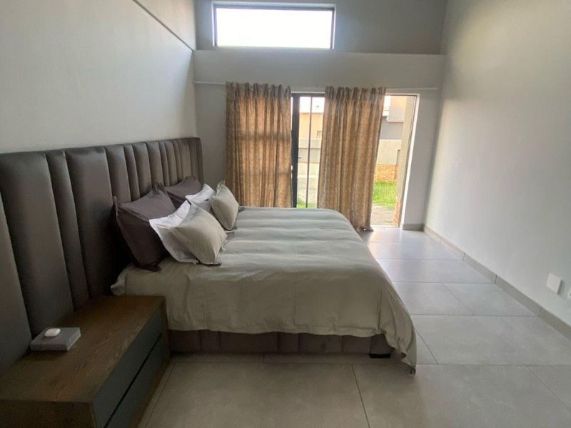 Spacious bedroom featuring high ceilings, large format floor tiles, a clerestory window, and direct access to the exterior through a sliding glass door.