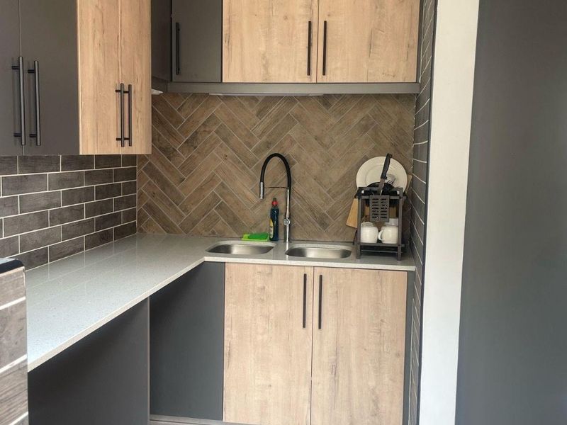 A modern, compact scullery featuring stone countertops, dual sinks, and a stylish herringbone tile splashback with contemporary two-tone cabinetry.