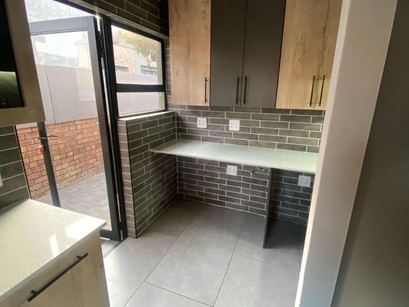 A modern, well-maintained scullery featuring contemporary two-tone cabinetry, stone countertops, subway tile backsplash, and direct access to an outdoor paved area.